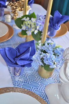 the table is set with blue flowers and gold place settings for an elegant dinner party