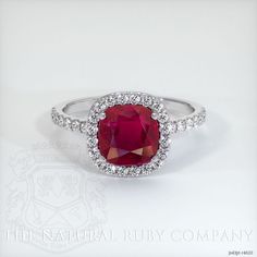 a ring with a large red stone surrounded by white diamonds on the sides and an oval halo around it