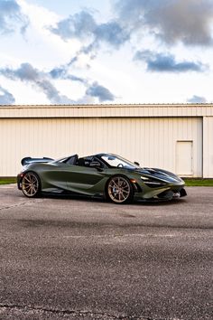 a green sports car parked in front of a white building with dark clouds above it