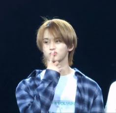 a young man with his finger in his mouth while standing next to another person wearing a blue and white checkered shirt