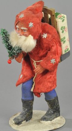 a santa clause figurine holding a christmas tree in his right hand and looking at the camera