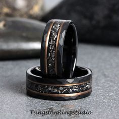 two wedding bands with black and gold inlays are on top of each other