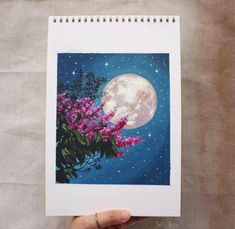 a person holding up a painting with flowers in front of the moon