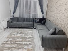 a living room with grey couches and white curtains on the window sill next to a rug