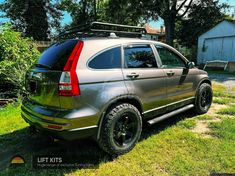 the back end of a silver suv parked on grass in front of a barn and trees