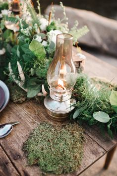 an arrangement of greenery on a wooden table with silverware and candlesticks