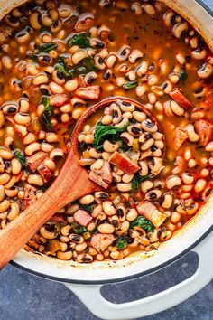 a wooden spoon in a pot filled with black - eyed beans and spinach soup