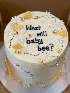 a white cake with yellow and white flowers on it that says, what will baby bee?