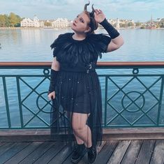 a woman in a black dress is standing on a pier near the water with her hands behind her head