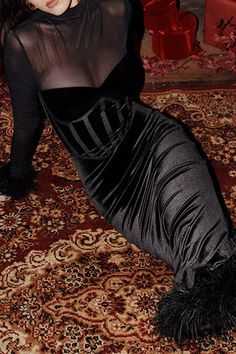 a woman in a black dress laying on top of a rug next to a christmas tree