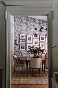 a dining room table and chairs in front of a wall with pictures hanging on it