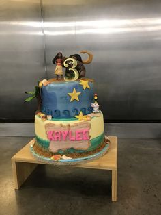 a three tiered birthday cake decorated with cartoon characters and stars on the top, sitting on a wooden table