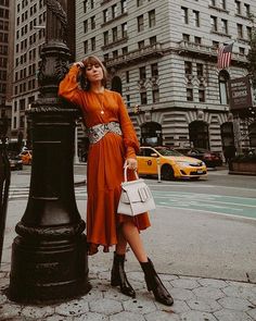 a woman in an orange dress leaning against a lamp post