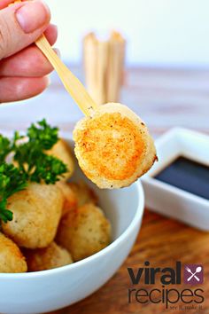 a hand holding a small piece of bread with parsley in it and dipping sauce on the side