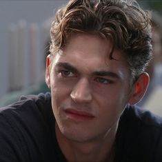 a close up of a person wearing a black shirt and looking at the camera with a serious look on his face