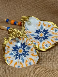 an orange, blue and white flowered glass dish with beaded handles sits on a brown cloth