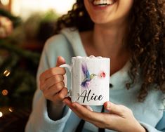 a woman holding a coffee mug with a humming bird on it and the words alice painted on it