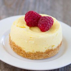 two raspberries on top of a cheesecake on a white plate with wood table