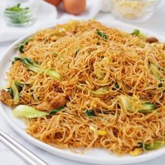 a white plate topped with noodles and veggies next to eggs on a table