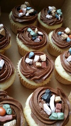 many cupcakes with chocolate frosting and candy on top are in a box