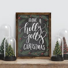 a christmas sign with snow globes and small trees in front of it on top of a shelf