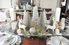 a dining room table decorated for christmas with silver and white decorations, candles and deer figurines