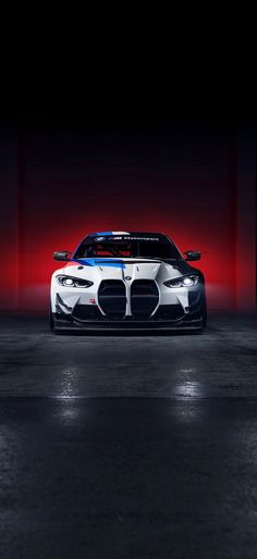 a white and blue sports car parked in a dark room with red light behind it