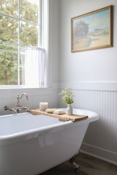 a white bath tub sitting under a window next to a wooden tray with flowers in it