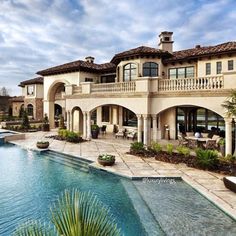 an outdoor swimming pool surrounded by lounge chairs and palm trees in front of a large house