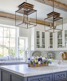 a kitchen with white cabinets and lots of flowers on the counter top in front of two windows