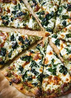 a pizza with spinach and cheese cut into four slices on a cutting board,