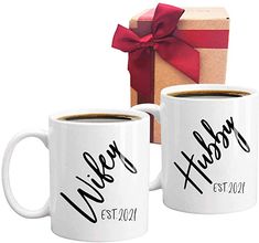 two coffee mugs sitting next to each other with a gift box in the background