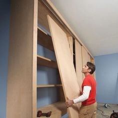 a man standing next to a book shelf holding a large piece of wood on top of it