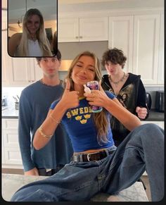 two people are sitting on the kitchen counter and one is taking a selfie with her cell phone