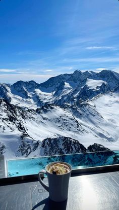 a cup of coffee sitting on top of a glass table next to a mountain range