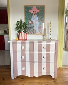 a pink and white striped dresser with a painting on the wall behind it in a living room