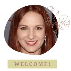 a woman with long red hair smiling at the camera in front of a welcome sign