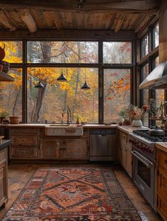 a kitchen with an area rug on the floor and large windows overlooking trees in autumn