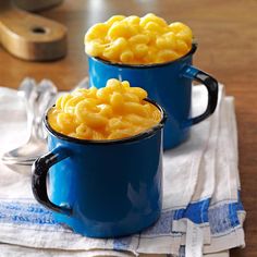 two blue mugs filled with macaroni and cheese on top of a table