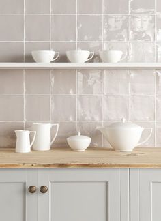 white dishes are lined up on a shelf above the kitchen counter, and below it is a tile backsplash