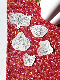 some paper cut outs sitting on top of a red cloth with white flowers and butterflies