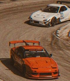 two race cars driving around a track during the day, one is orange and the other is white