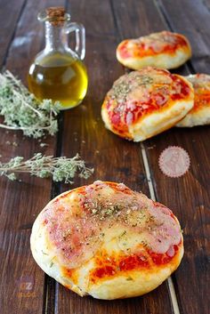 three small pizzas sitting on top of a wooden table next to olive oil and pepperoni