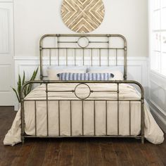 a metal bed frame in a white bedroom with wood flooring and large round mirror on the wall above it