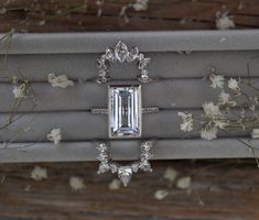 an engagement ring and wedding band sitting on top of a box with flowers in the background