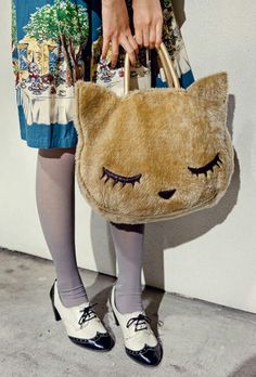 a woman is holding a cat purse with her eyes closed while standing in front of a wall