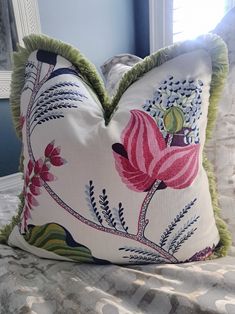 a white pillow with pink and green flowers on it sitting on top of a bed