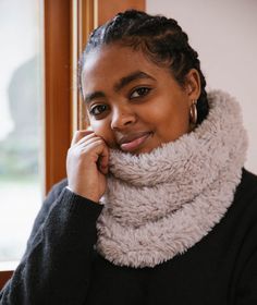 a woman with braids wearing a cowl neck scarf in front of a window