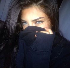 a close up of a person covering their face with a black shirt and blue eyes