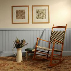 a rocking chair next to a vase with flowers in it and two framed pictures on the wall